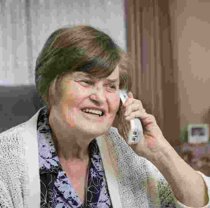 An older adult sitting on a couch on her phone with a smile of their face.
